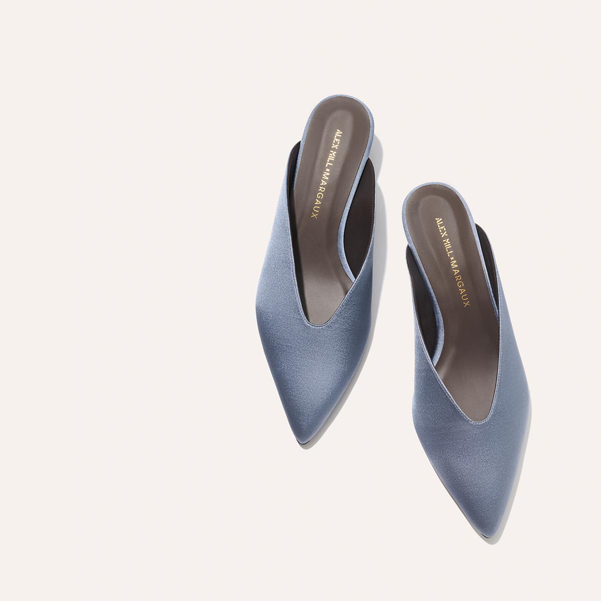 A pair of Margaux Alex Mill x Margaux: The Romy - Slate Blue Satin pointed-toe, slip-on kitten mules with gold ALBERTO MARANGONI on the insole, shown on a light, neutral background.