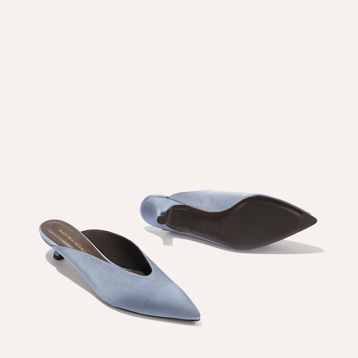 The Margaux Alex Mill x Margaux: The Romy - Slate Blue Satin kitten mules feature pointed toes and low heels; shown on a plain background, one stands upright while the other reveals its sole—an elegant, comfortable choice for any occasion.