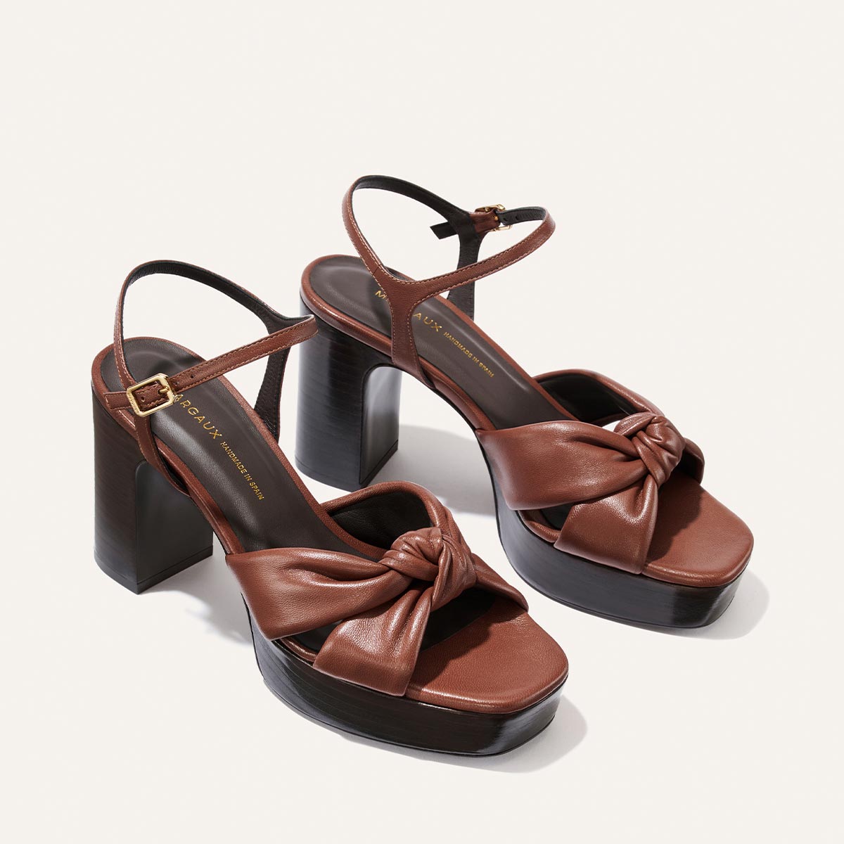 The Sabine Platform by Margaux in Brandy Glove Nappa features high block heels, knotted leather straps across the toes, ankle straps with small buckle closures, and dark chunky soles, displayed on a light background.
