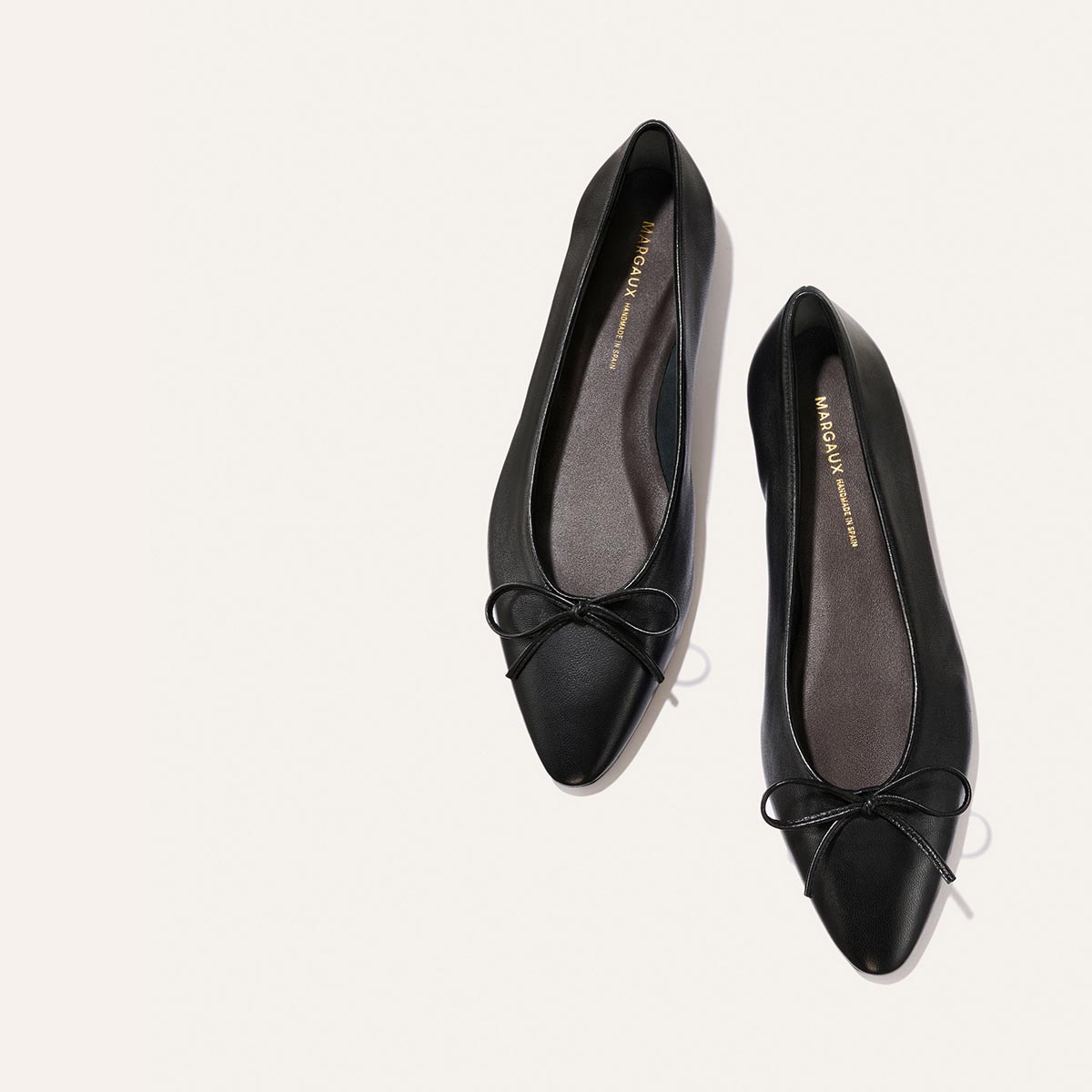 The Salamanca - Black Nappa by Margaux: buttery soft black leather pointed-toe ballet flats with delicate bows, featured on a light-colored background.