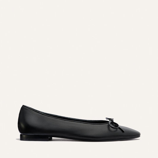 The Salamanca - Black Nappa by Margaux is a black ballet flat with a small bow detail on the rounded toe, shown in side profile against a plain white background.