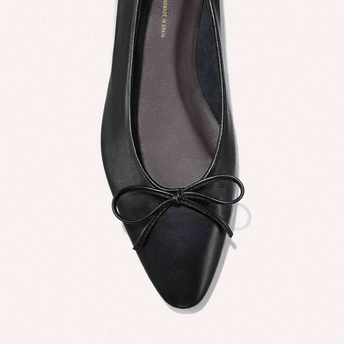 The Salamanca - Black Nappa by Margaux: a black pointed-toe flat in soft leather with a small bow detail, shown from above on a light background.