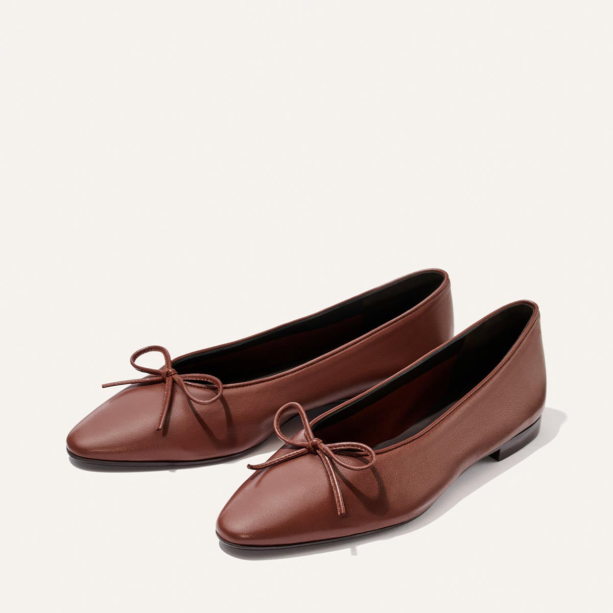 A pair of elegant shoes, Margaux’s The Salamanca - Brandy Nappa ballet flats feature rounded toes and decorative bows on the front, set against a light background.