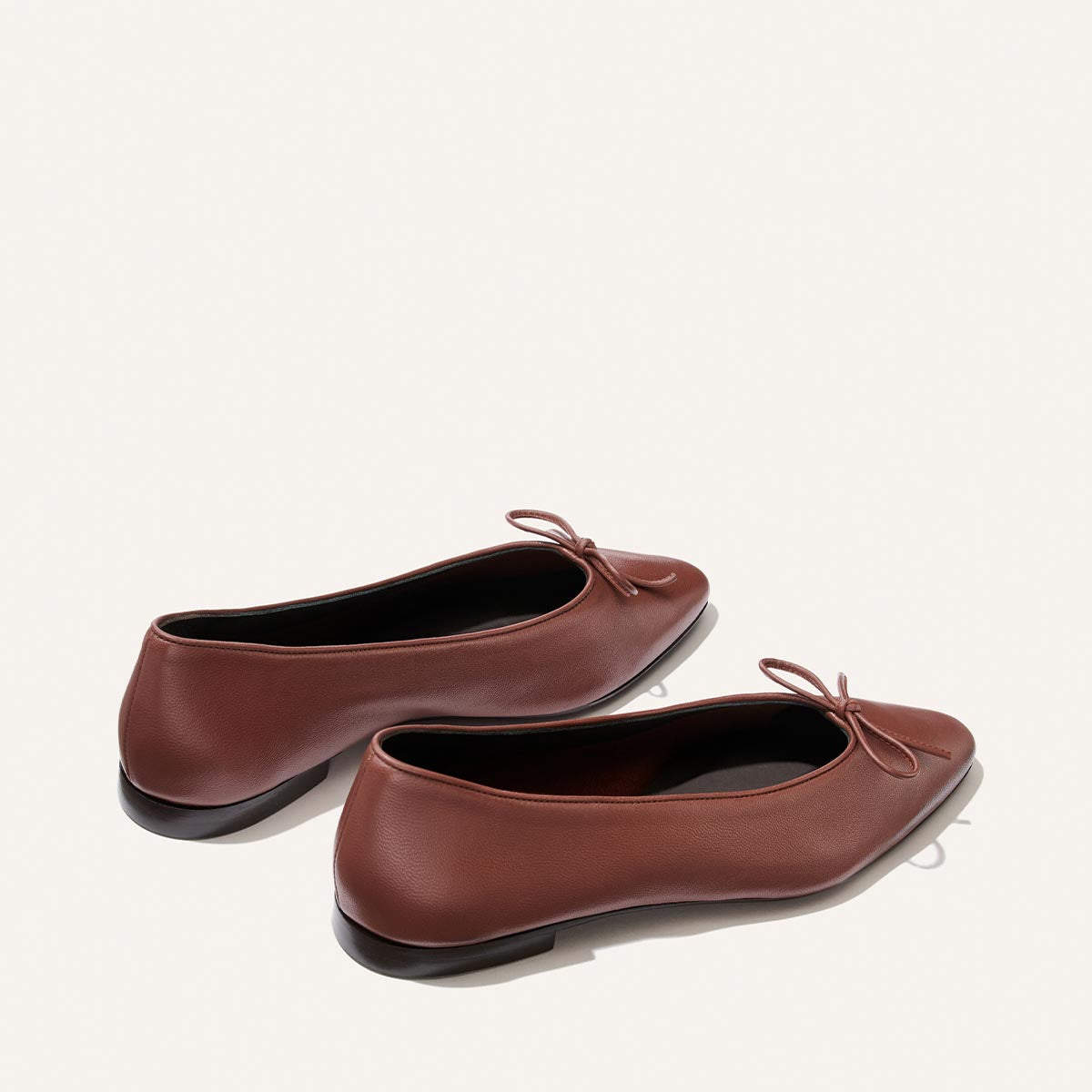 The Salamanca - Brandy Nappa by Margaux is a pair of elegant brown leather pointed toe ballet flats, featuring small bows on the front and displayed on a light background—these shoes effortlessly combine style and comfort.