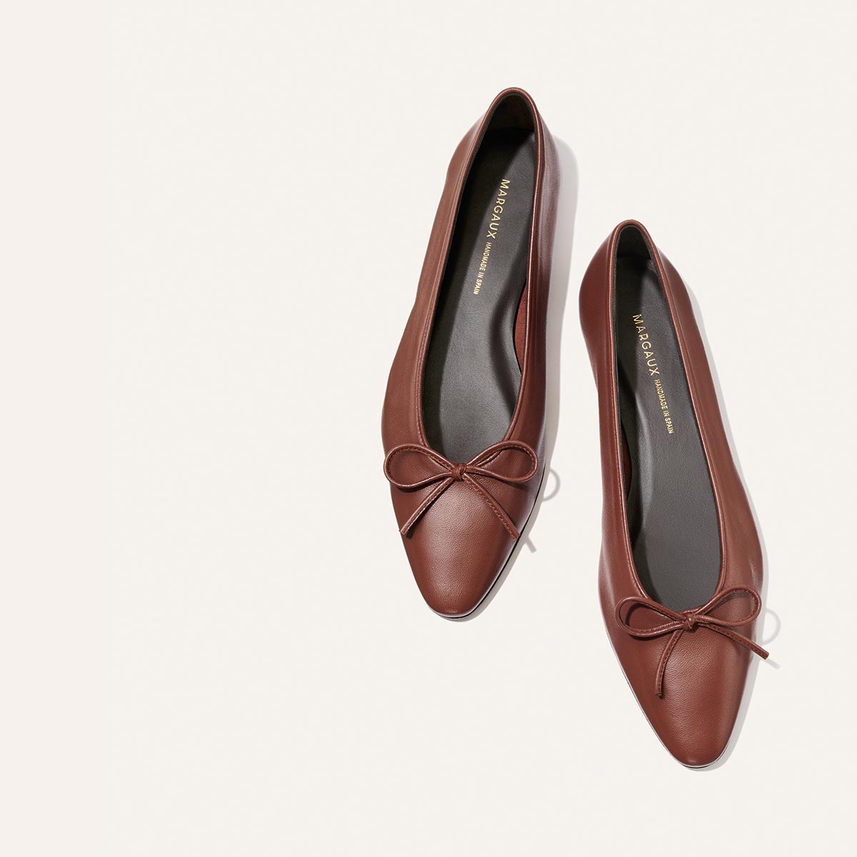 The Salamanca - Brandy Nappa by Margaux: brown buttery soft leather pointed-toe flats with bows, shown on a light beige background.