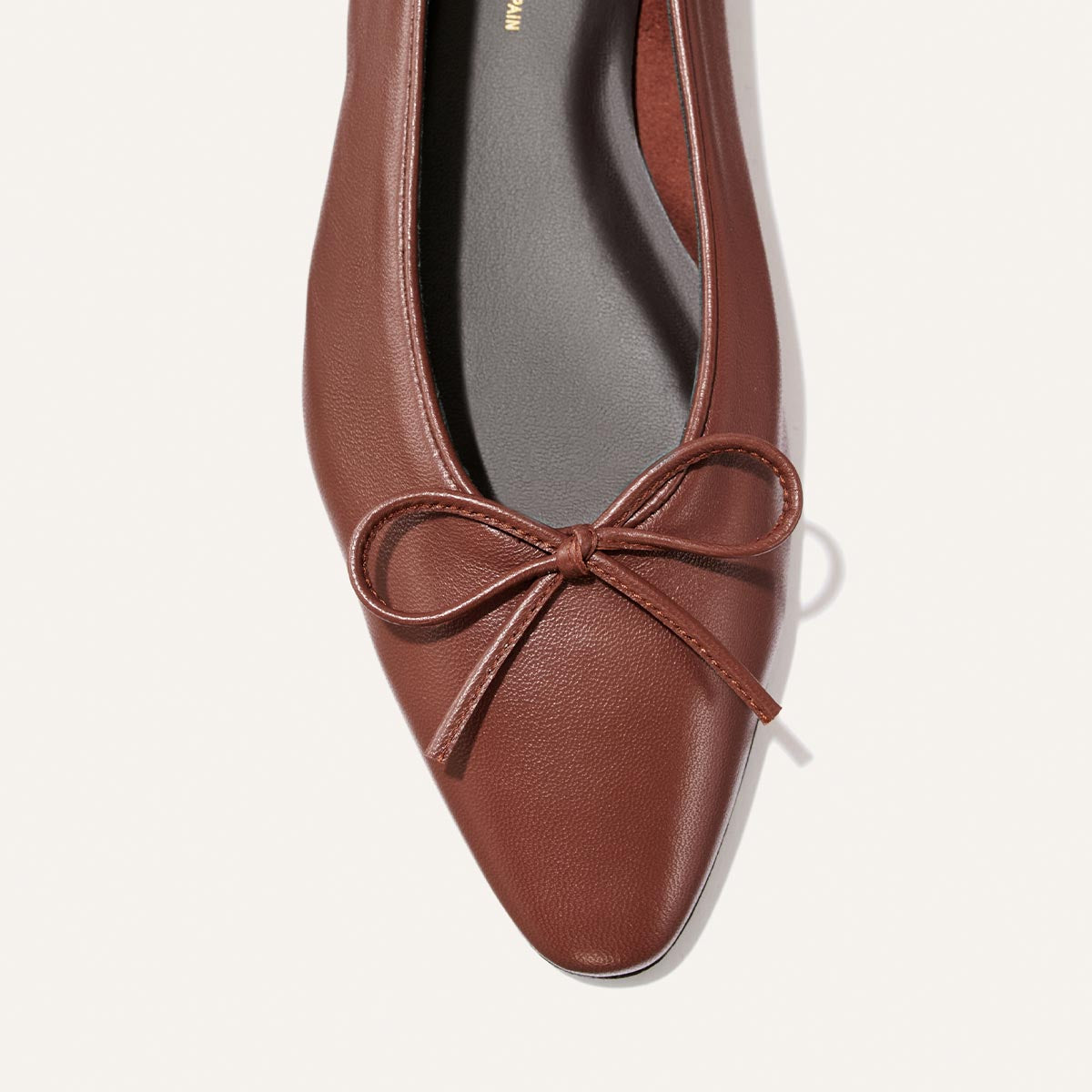 The Salamanca - Brandy Nappa by Margaux is an elegant brown leather ballet flat featuring a rounded square toe and a matching bow on the front. The shoe is designed with a black insole and is showcased against a light, neutral background.