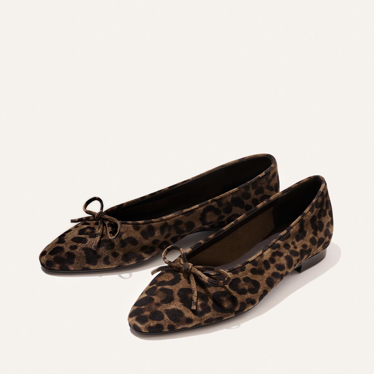 A pair of The Salamanca - Brown Leopard Suede ballet flats by Margaux, featuring leopard-print suede and small bows on the toes, displayed against a plain, light background.