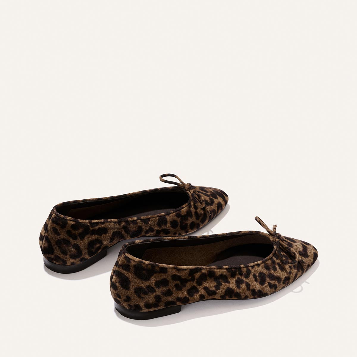 Two pairs of "The Salamanca - Brown Leopard Suede" ballet flats by Margaux, featuring small bows on the toe, are displayed against a plain white background to showcase both the side and back views of the shoes.