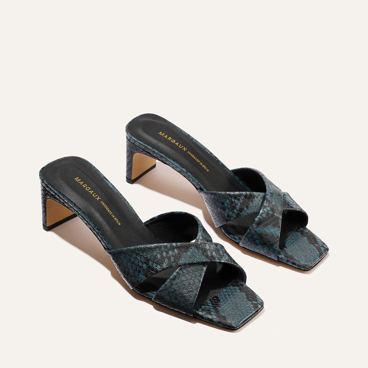 The Selene 50 by Margaux features aqua python-embossed heeled sandals with crisscross toe straps, square open toes, and a mid-height block heel.