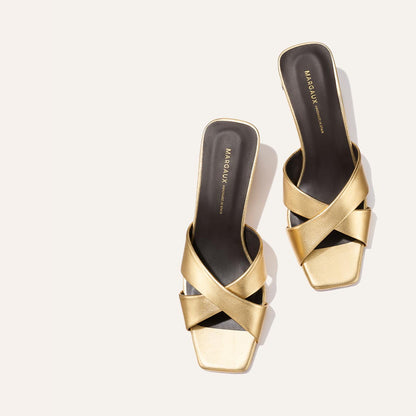 The Selene 50 - Gold Nappa by Margaux: gold open-toe slides with leather crisscross straps, square toes, and black insoles featuring the Margaux logo in gold, displayed on a light background.