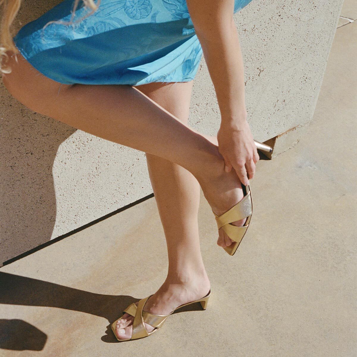 Person wearing gold high-heeled shoes on a concrete surface