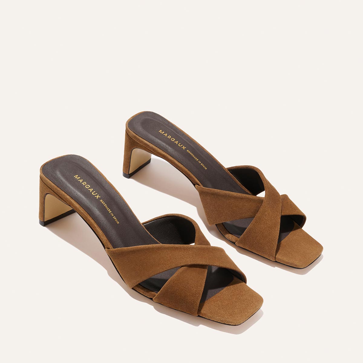 The Selene 50 - Nutmeg Suede by Margaux: brown suede open-toe slip-on heeled sandals with crisscross leather straps and a mid-height square block heel, displayed on a light background.