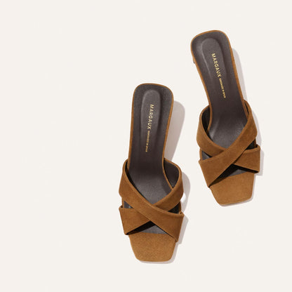 The Selene 50 - Nutmeg Suede by Margaux: brown suede slide sandals with leather crisscross straps, square toes, a subtle block heel, and dark insoles featuring the Margaux name in gold, shown on a light background.