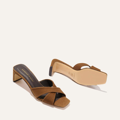 The Selene 50 - Nutmeg Suede by Margaux: brown suede slip-on heeled sandals with crisscross leather straps and a square block heel, shown with one shoe upright and the other on its side to display the sole.