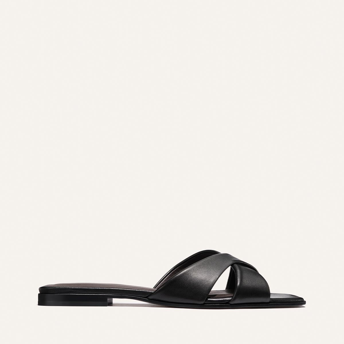 The Selene Flat Sandal by Margaux in Black Nappa features two wide, crisscrossed straps and a low heel, shown against a plain white background.