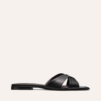 The Selene Flat Sandal by Margaux in Black Nappa features two wide, crisscrossed straps and a low heel, shown against a plain white background.