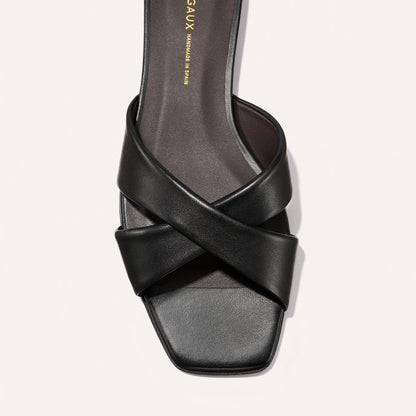 The Selene Flat Sandal by Margaux in Black Nappa features two wide, crisscrossed leather straps and a square open toe, shown from above against a light background.