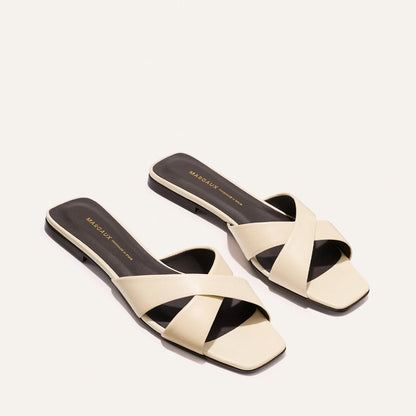 The Selene Flat Sandal - Ivoire Nappa by Margaux features beige wide crisscross straps, flat soles, and square toes, shown against a plain light background.