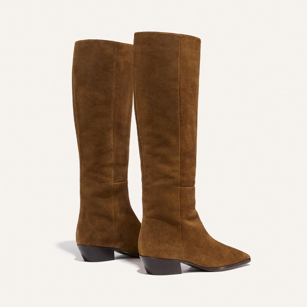 A pair of Margaux’s The Sierra Knee-High Boots in Cedar Suede, featuring low block heels and pointed toes, are standing side by side against a plain, light background.