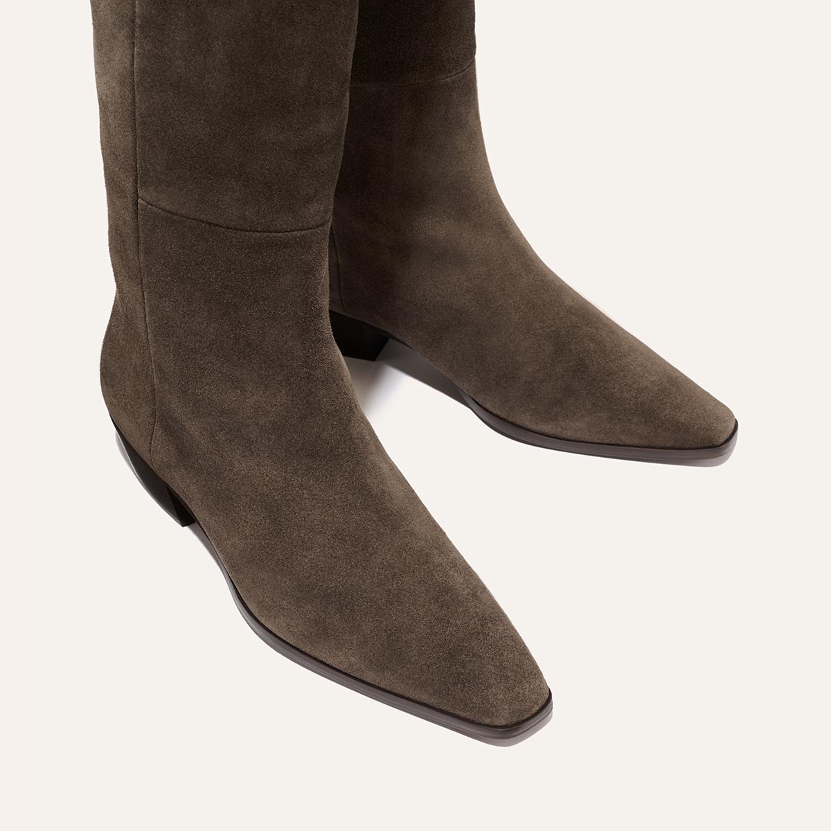 A close-up view of The Sierra Knee-High Boot in English Brown Suede by Margaux, featuring pointed toes and low heels, displayed on a light background.