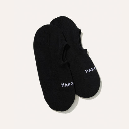 A pair of The Sneaker Sock - Black by Margaux, featuring non-slip grips and MARG embroidered in white near the toe, displayed on a plain light background.