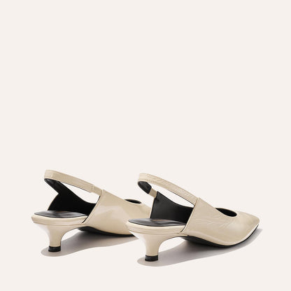 The Sofia Sling - Ecru Crinkle Patent by Margaux are beige, low-heeled slingbacks with pointed toes and black inner soles, featuring a subtle micro heel. They’re shown on a light background, facing away from the camera.