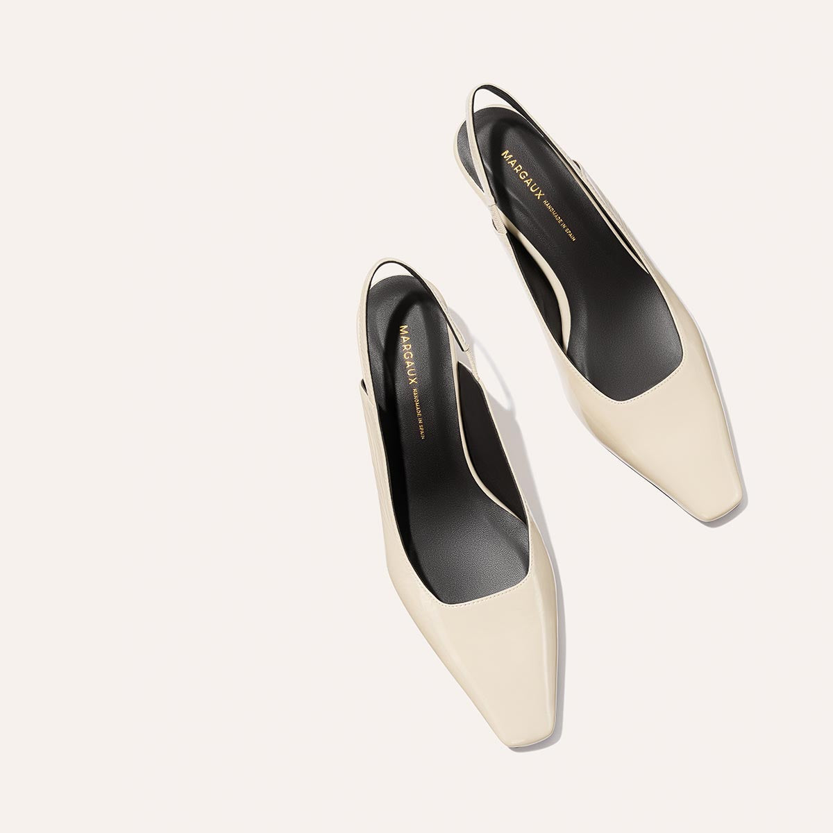 A pair of ecru crinkle patent Sofia Sling shoes by Margaux, featuring a square toe, subtle micro heel, black insoles with gold ‘Margaux’ branding—displayed on a light background.
