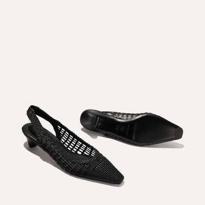 Two black woven leather Sofia Sling shoes by Margaux are displayed on a light background; one stands upright while the other lies on its side, revealing the sole and showcasing their elegant low-heeled slingback design.
