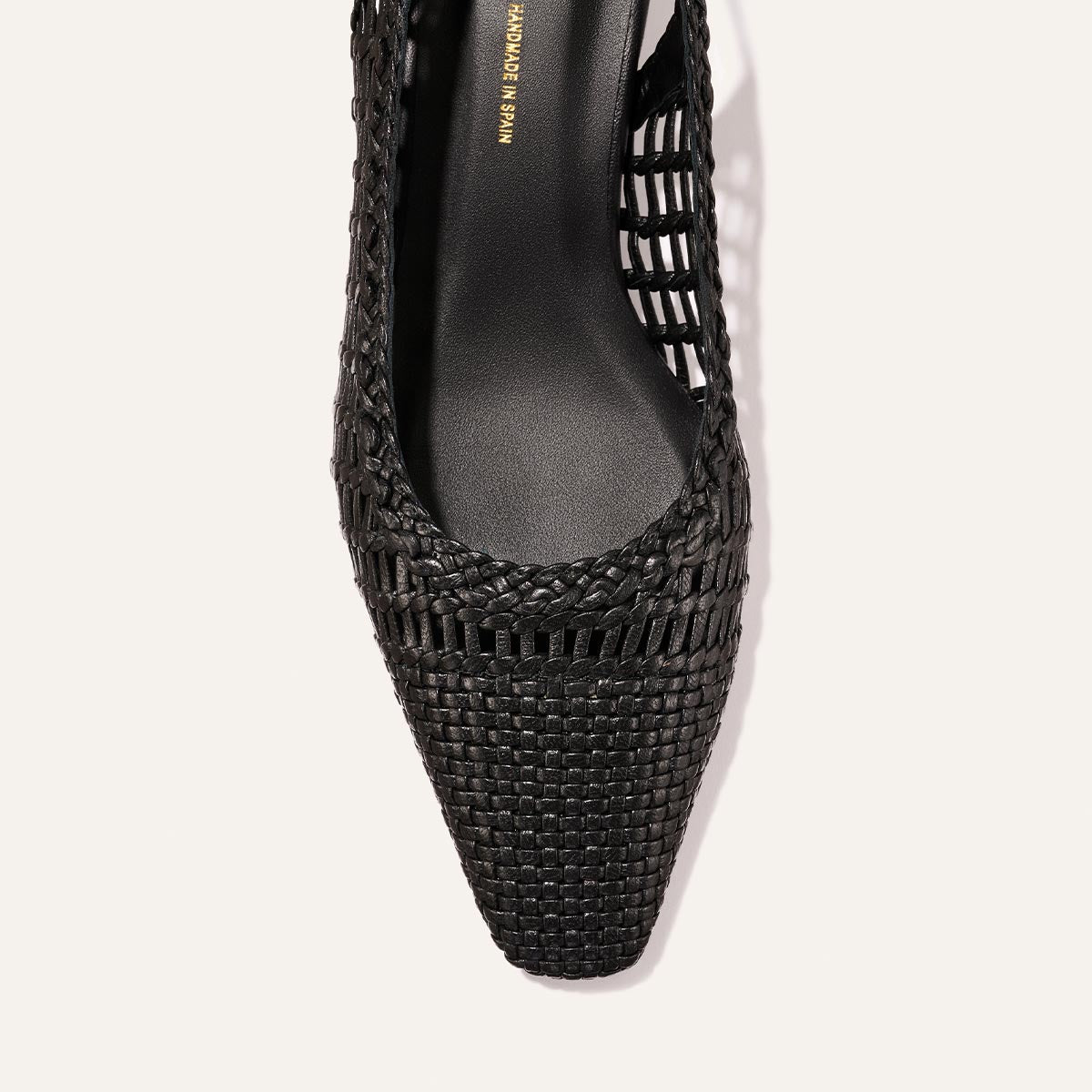 Close-up of The Sofia Sling by Margaux in black woven leather, featuring a pointed square toe and cutout sides, viewed from above on a light background.