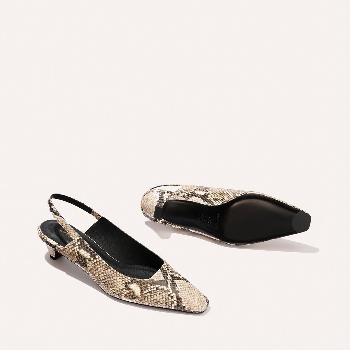The Sofia Sling - Natural Python Embossed by Margaux, a pair of women's slingback kitten heels with a snip toe and 1.5" heel, featuring a beige and brown python-embossed pattern, is displayed on a plain white background. One shoe is upright while the other lies on its side to show the sole.