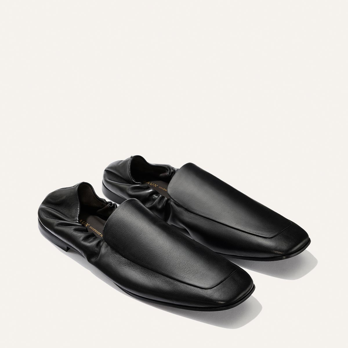 A pair of The Studio Loafer - Black Nappa by Margaux, crafted in black leather with a minimalist design, square toe, and gathered heel detail, placed on a light background.