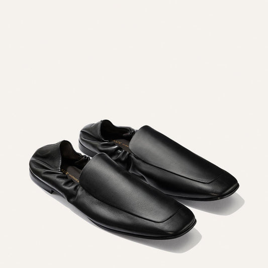 A pair of The Studio Loafer - Black Nappa by Margaux, crafted in black leather with a minimalist design, square toe, and gathered heel detail, placed on a light background.