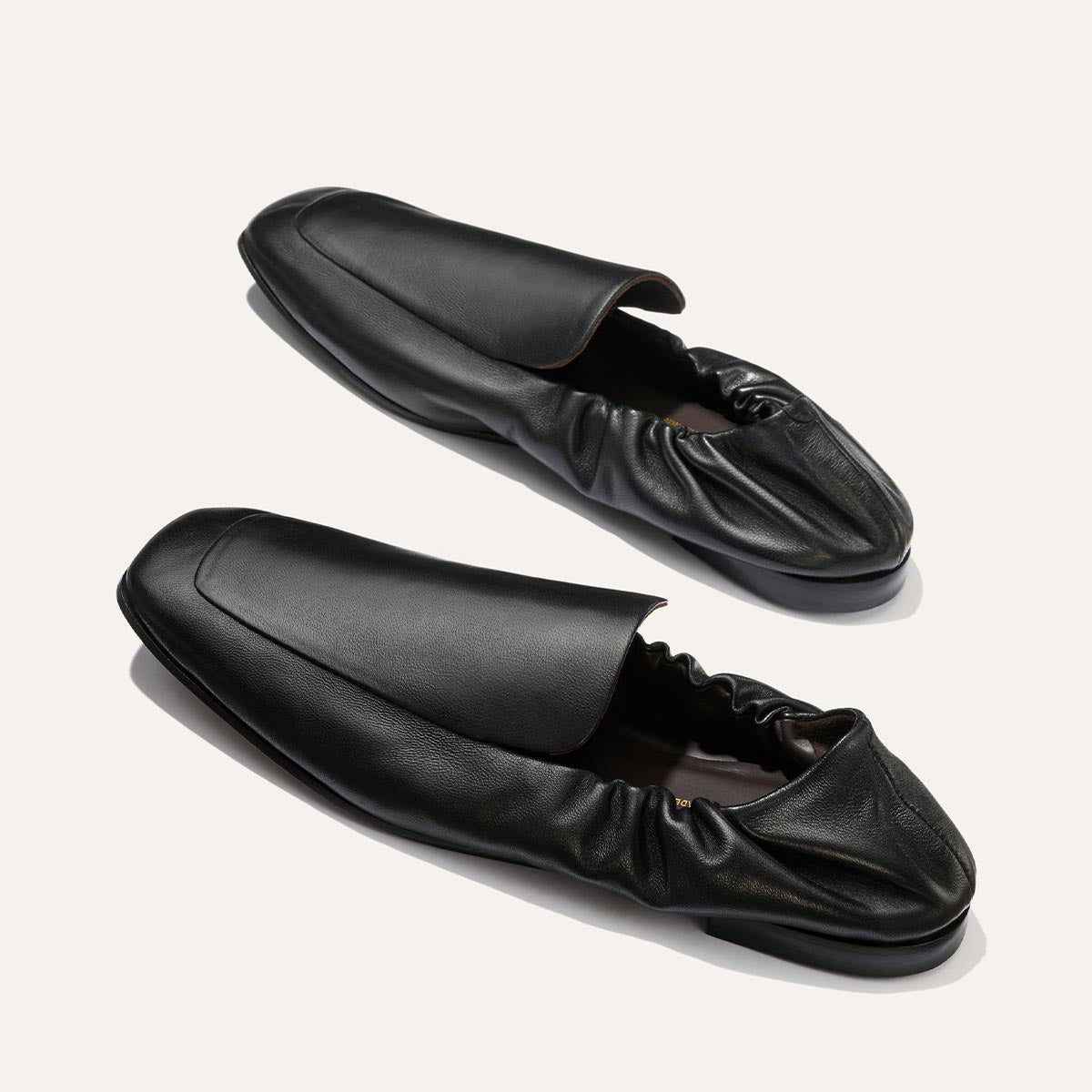 A pair of Margaux's The Studio Loafer in Black Nappa, featuring ruched elastic backs, displayed on a light background.