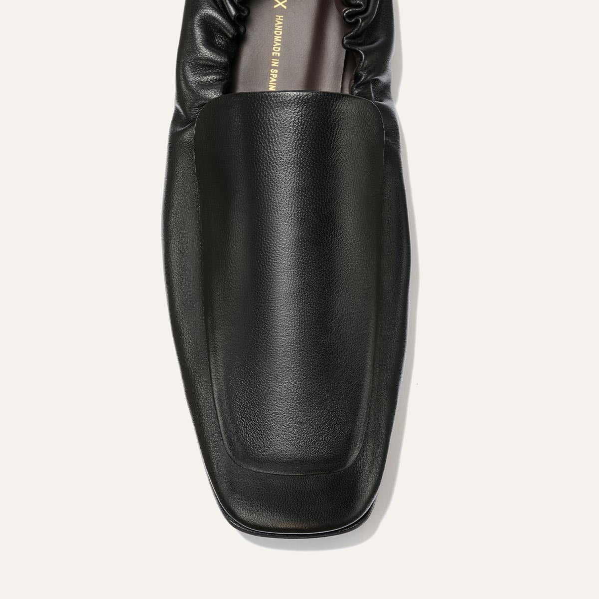A top view of Margaux’s The Studio Loafer in Black Nappa, featuring a square toe and gathered elastic detail at the heel, displayed against a plain light background.