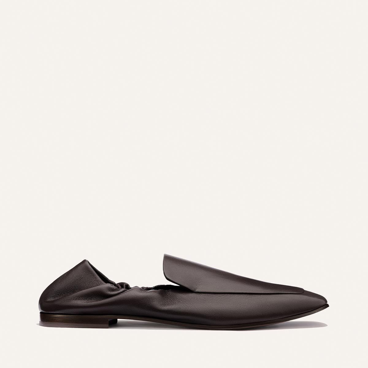 A side view of The Studio Loafer - Espresso Nappa by Margaux, a single dark brown leather slip-on featuring a slightly wrinkled texture, flat sole, and a minimalist, modern design on a plain light background.