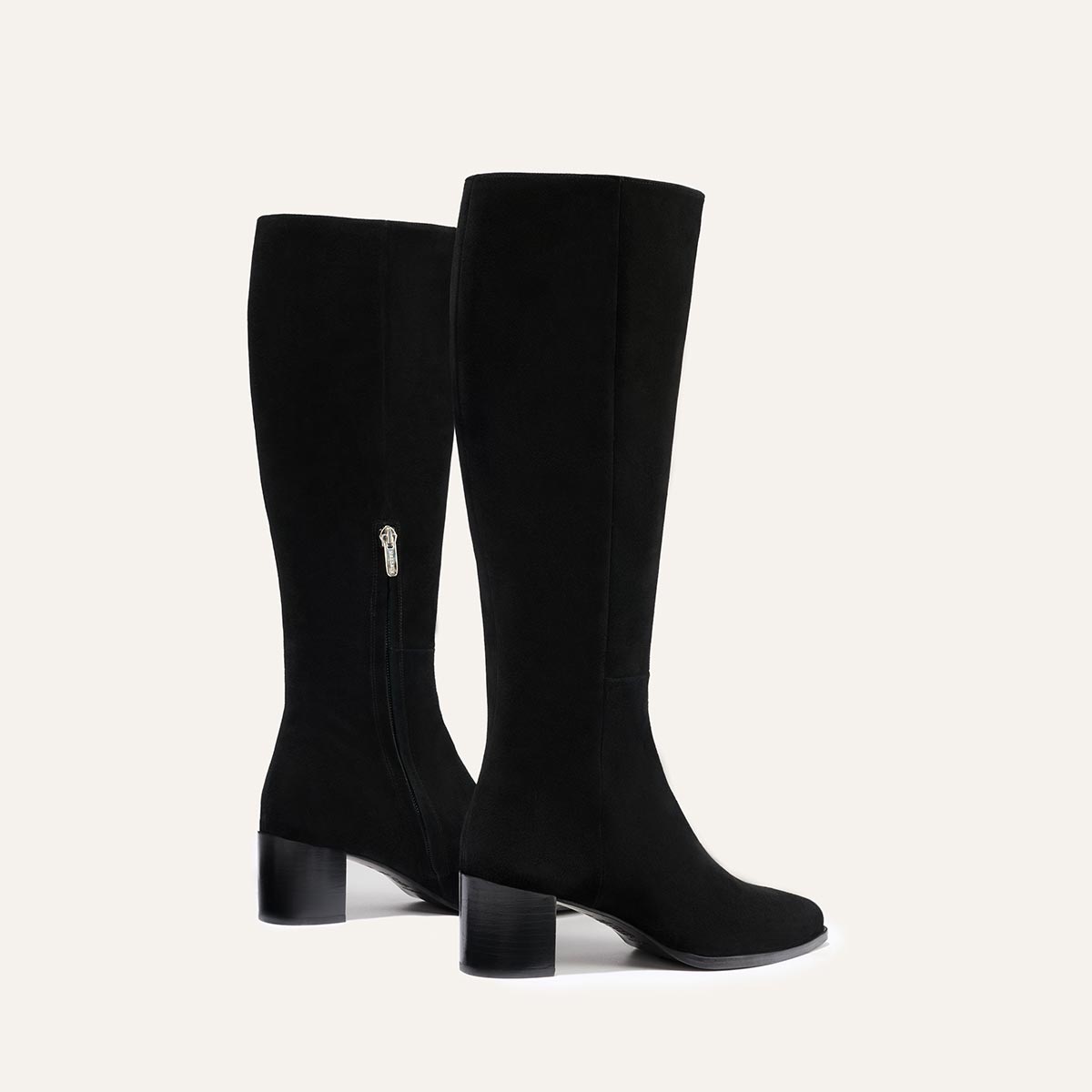 The Uptown Boot - Black Suede by margaux-development: black knee-high boots with low block heels and side zippers, shown against a plain light background.