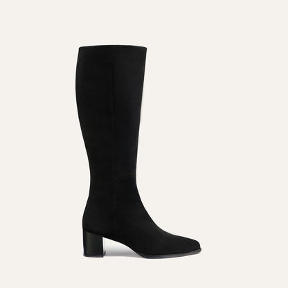 The Uptown Boot - Black Suede by margaux-development is a black knee-high boot with a block heel, crafted from suede-like material and displayed in profile against a light beige background.