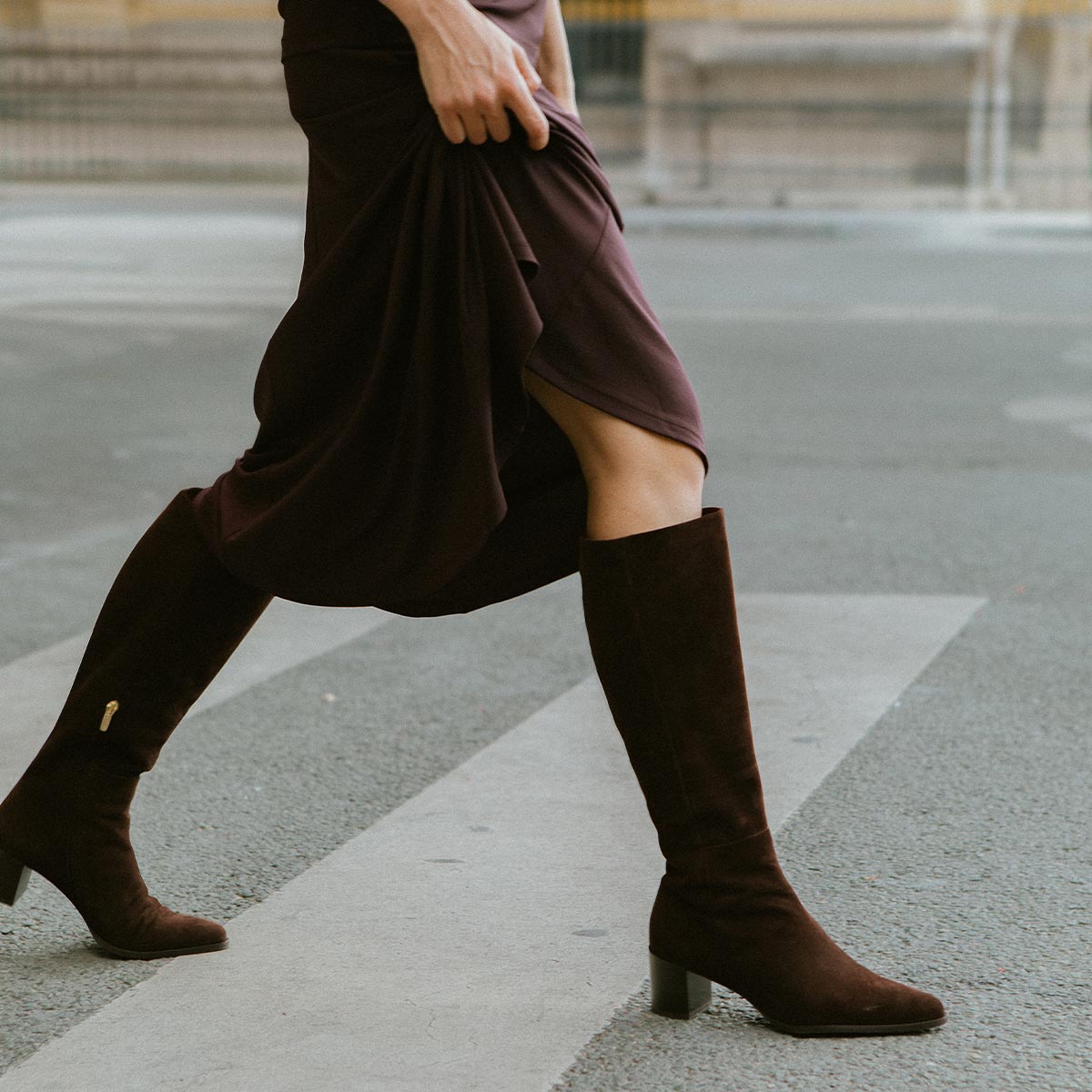 Person wearing brown knee-high boots and a dark skirt on a street.