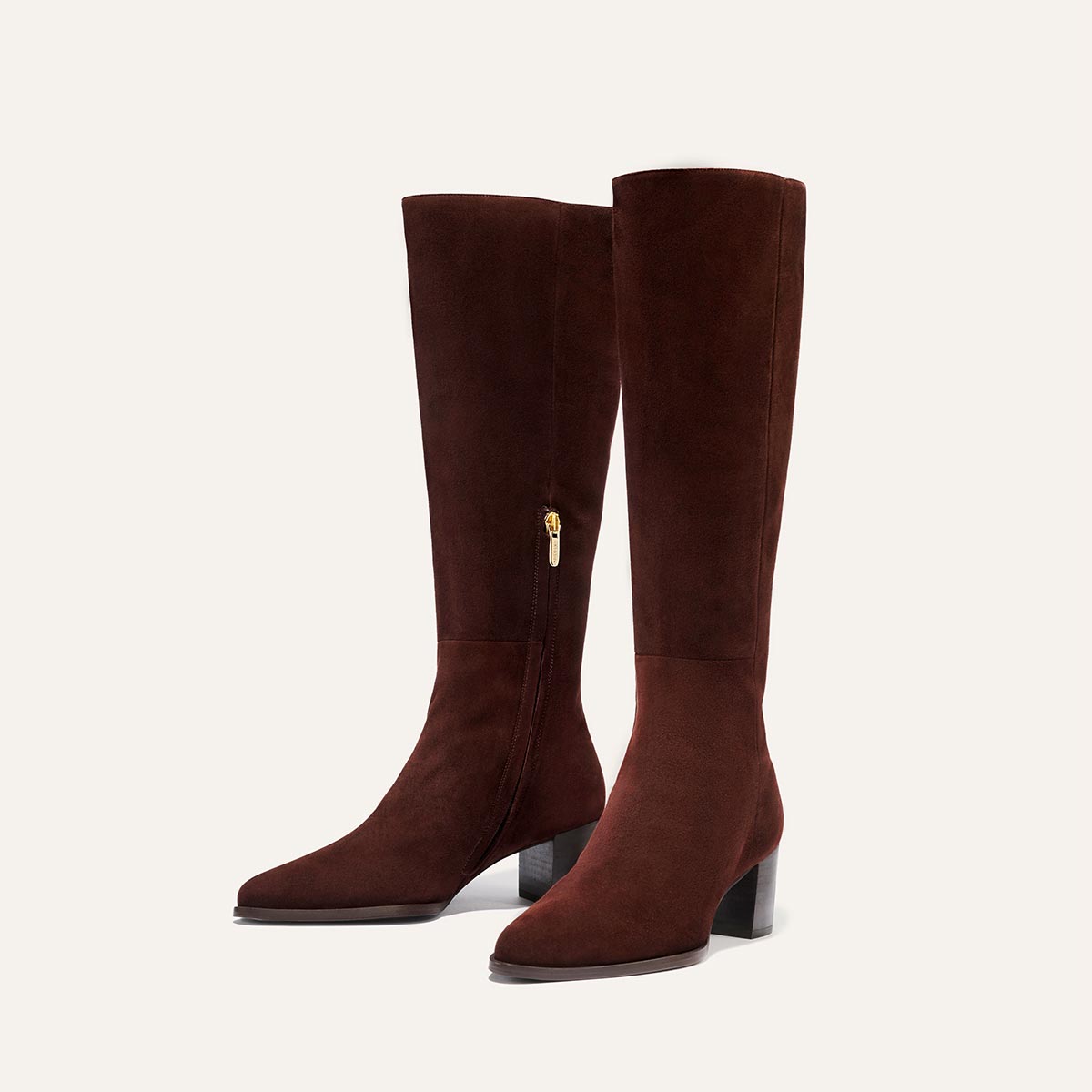 The Uptown Boot - Chocolate Suede by margaux-development: knee-high brown suede boots with mid-block heels and side zippers, inspired by the bestselling ankle boot style, shown against a light beige background.