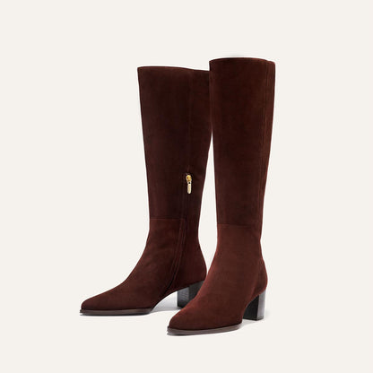 The Uptown Boot - Chocolate Suede by margaux-development: knee-high brown suede boots with mid-block heels and side zippers, inspired by the bestselling ankle boot style, shown against a light beige background.