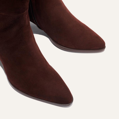 Close-up of The Uptown Boot by margaux-development, a bestselling ankle boot in chocolate suede with a pointed toe, shown against a light background.