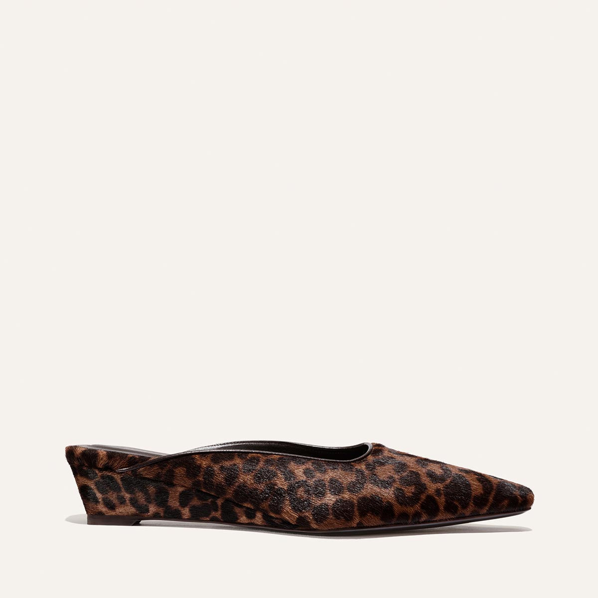 A side view of The Vesper Mule - Chocolate Leopard Haircalf by Margaux, a women’s flat slip-on shoe featuring a short wedge heel and a chocolate and black leopard print pattern, displayed on a plain off-white background.