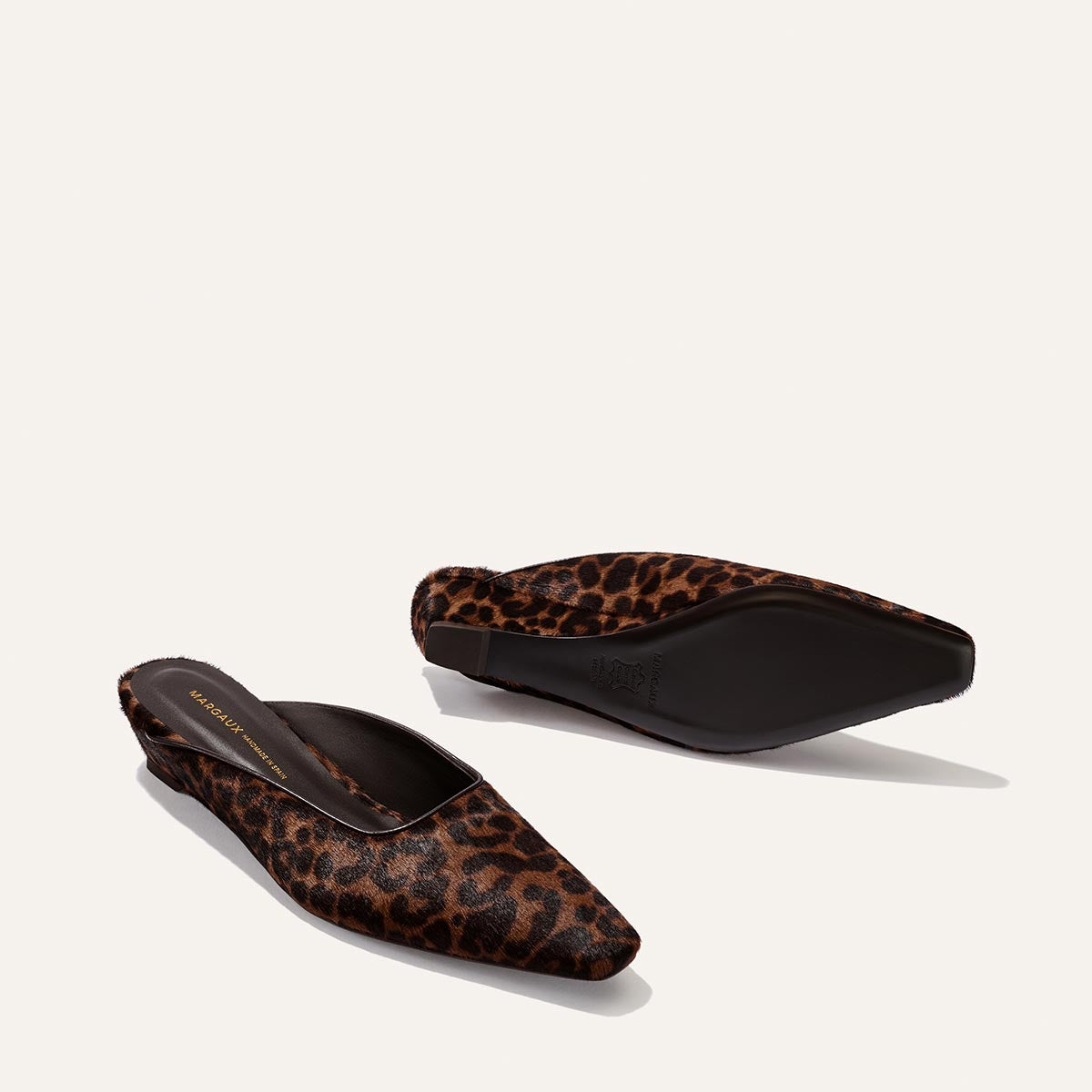 Two pointed-toe Vesper Mules by Margaux in Chocolate Leopard Haircalf. One shoe stands upright, revealing the top and inner sole, while the other rests on its side to display the sole.