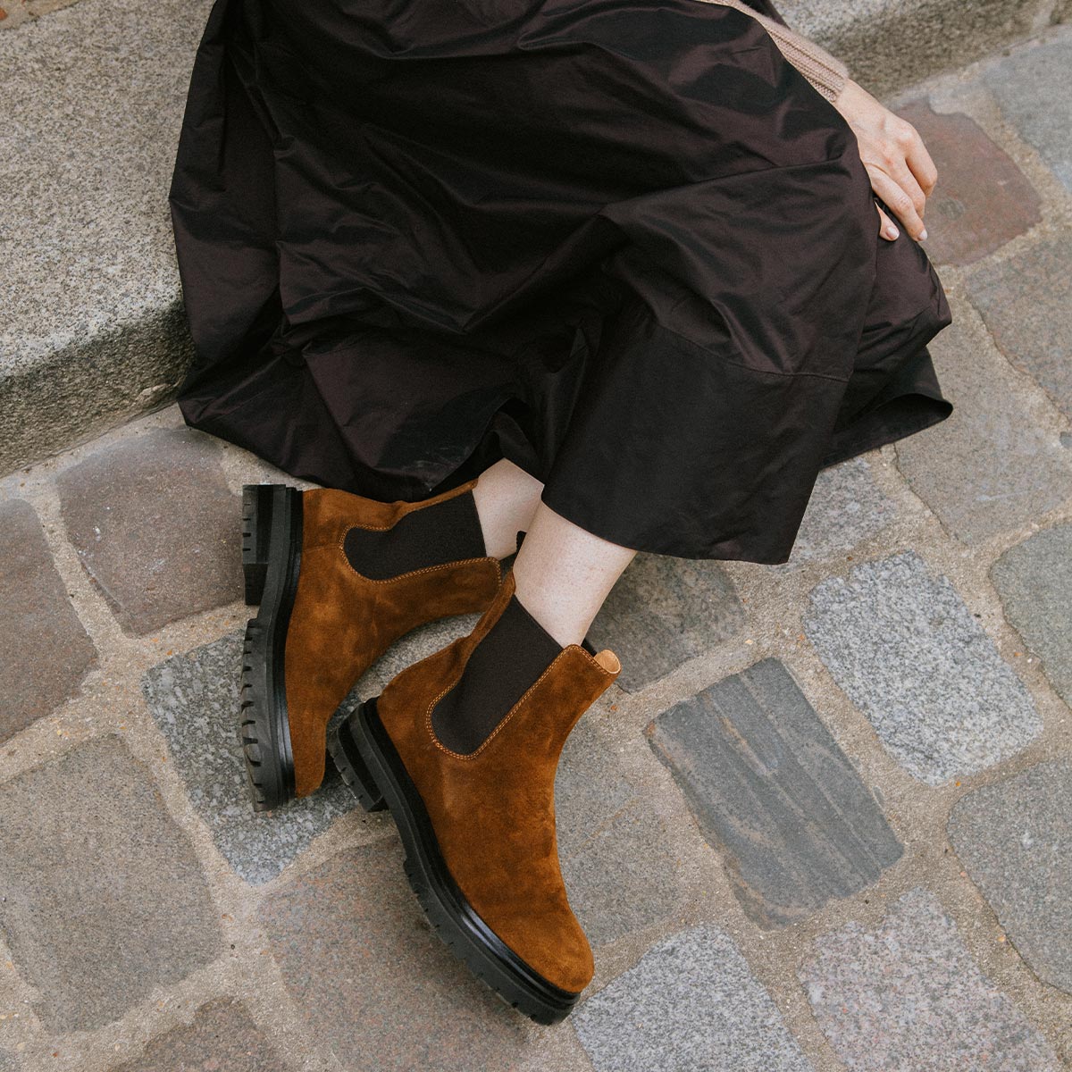 Person wearing brown suede boots on a stone pavement