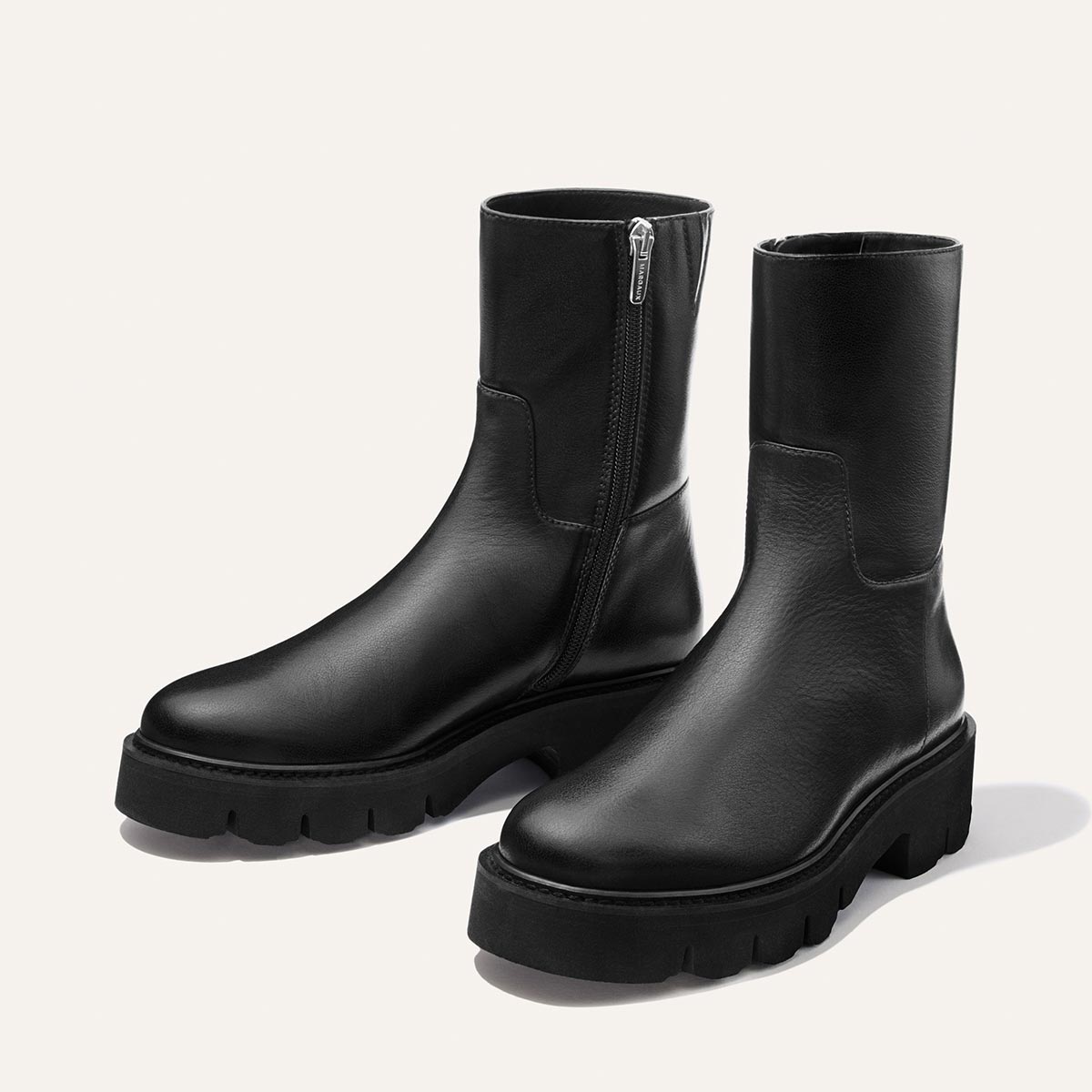 A pair of Margaux’s “The Wells Boot - Black Calf” ankle boots, featuring chunky rubber soles and side zippers, displayed on a light background.