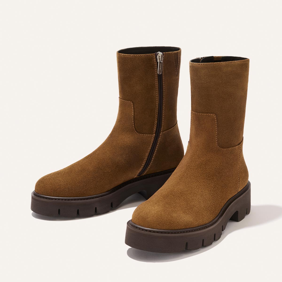 The Wells Boot in Cedar Suede by Margaux—a pair of mid-calf brown suede boots featuring chunky dark soles and side zippers—is displayed on a plain light background.