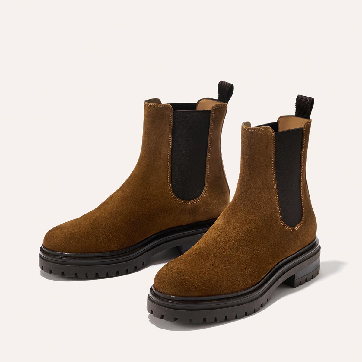 The Margaux West Chelsea Boot in Cedar Suede features black elastic side panels, back pull tabs, and a durable lug sole, shown on a light background.