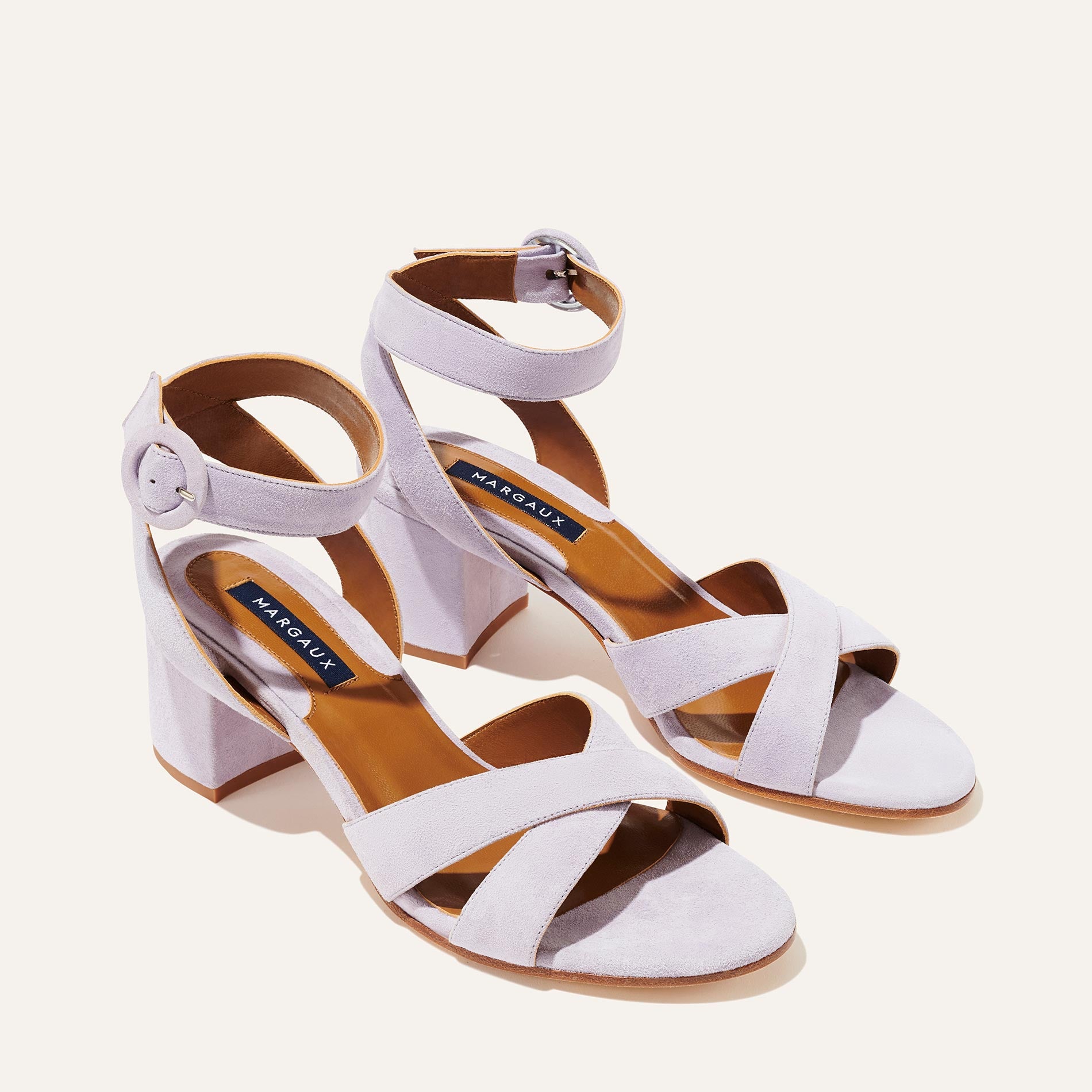 The City Sandal - Lilac Suede by margaux-development features light lavender suede, block heels, crisscross and adjustable ankle straps with round buckles, and a cushioned insole for comfort, shown on a light background.