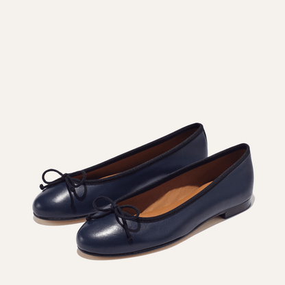 The Demi in Navy Nappa with black trim, a comfortable ballet flat with a rounded toe and adjustable cord bow detail.