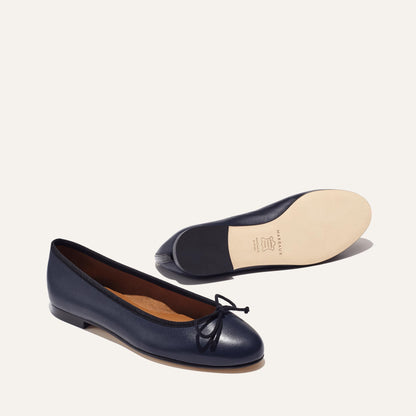 The Demi in Navy Nappa with black trim, a comfortable ballet flat with a rounded toe and adjustable cord bow detail.